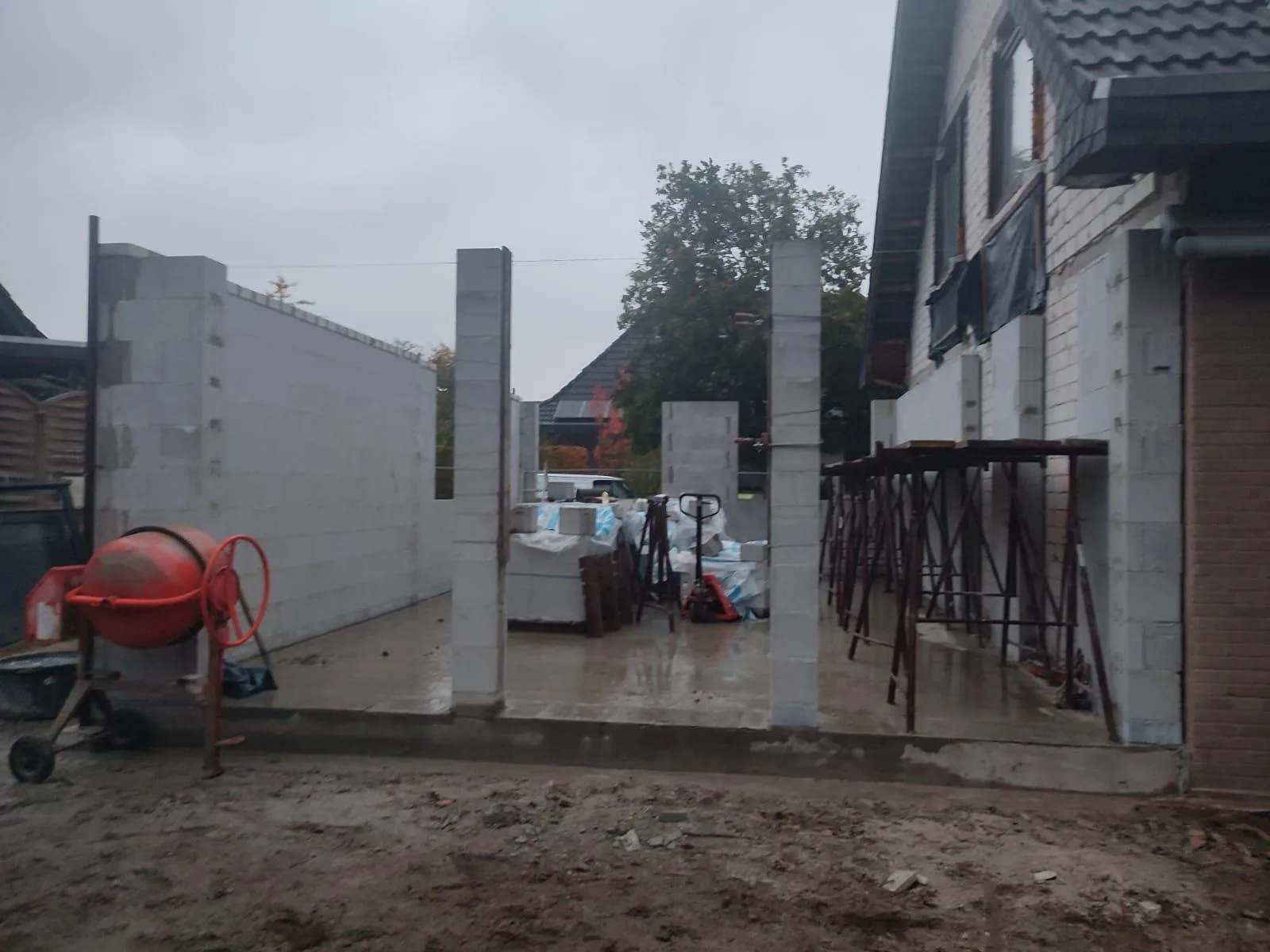 Rohbau eines Anbaus bei Regen mit Betonstützen und Betonmischer